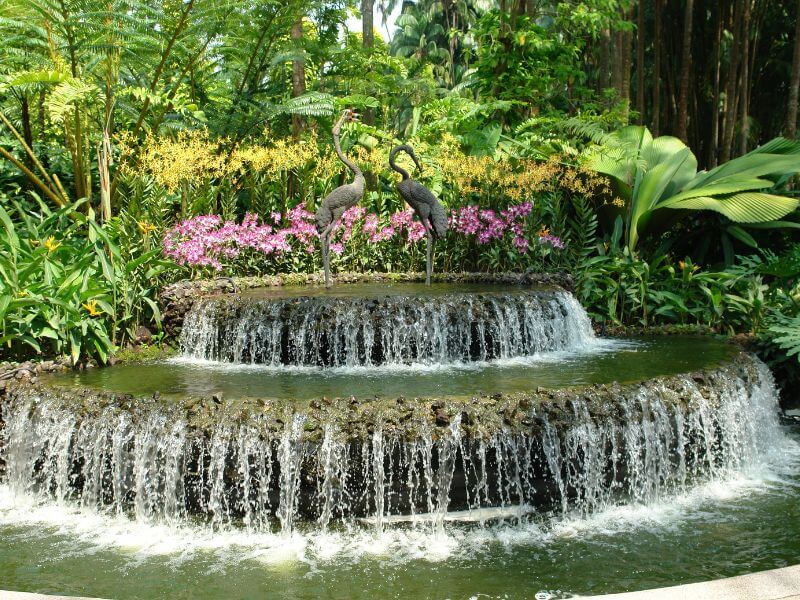 Two-tier waterfall fountain surrounded by flowers and plants