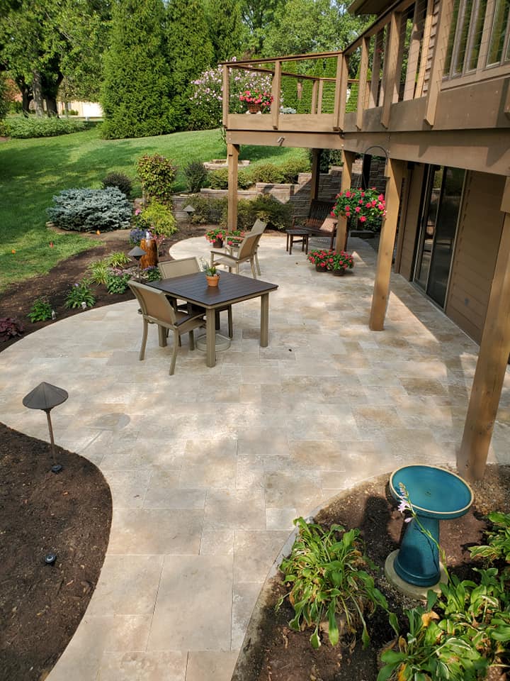 Stone patio under a raised deck with a dining table and planters