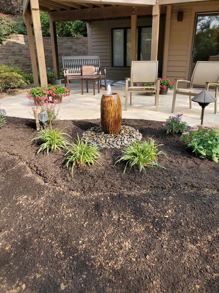 Small fountain in a new garden bed beside a covered patio