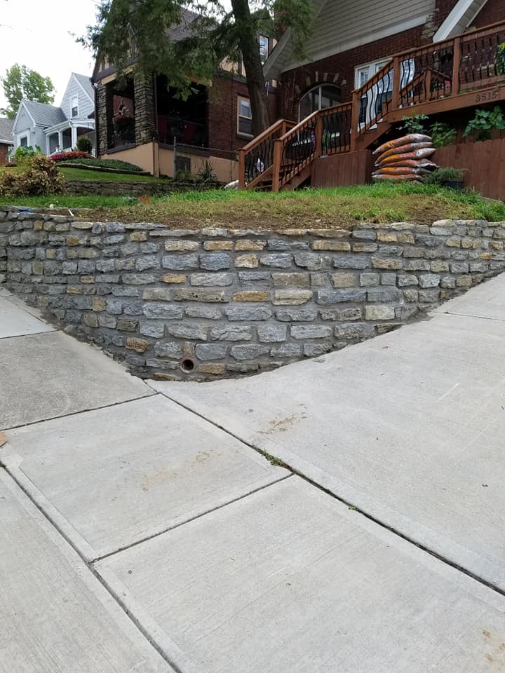 Stone retaining wall along a sloped sidewalk below a front yard