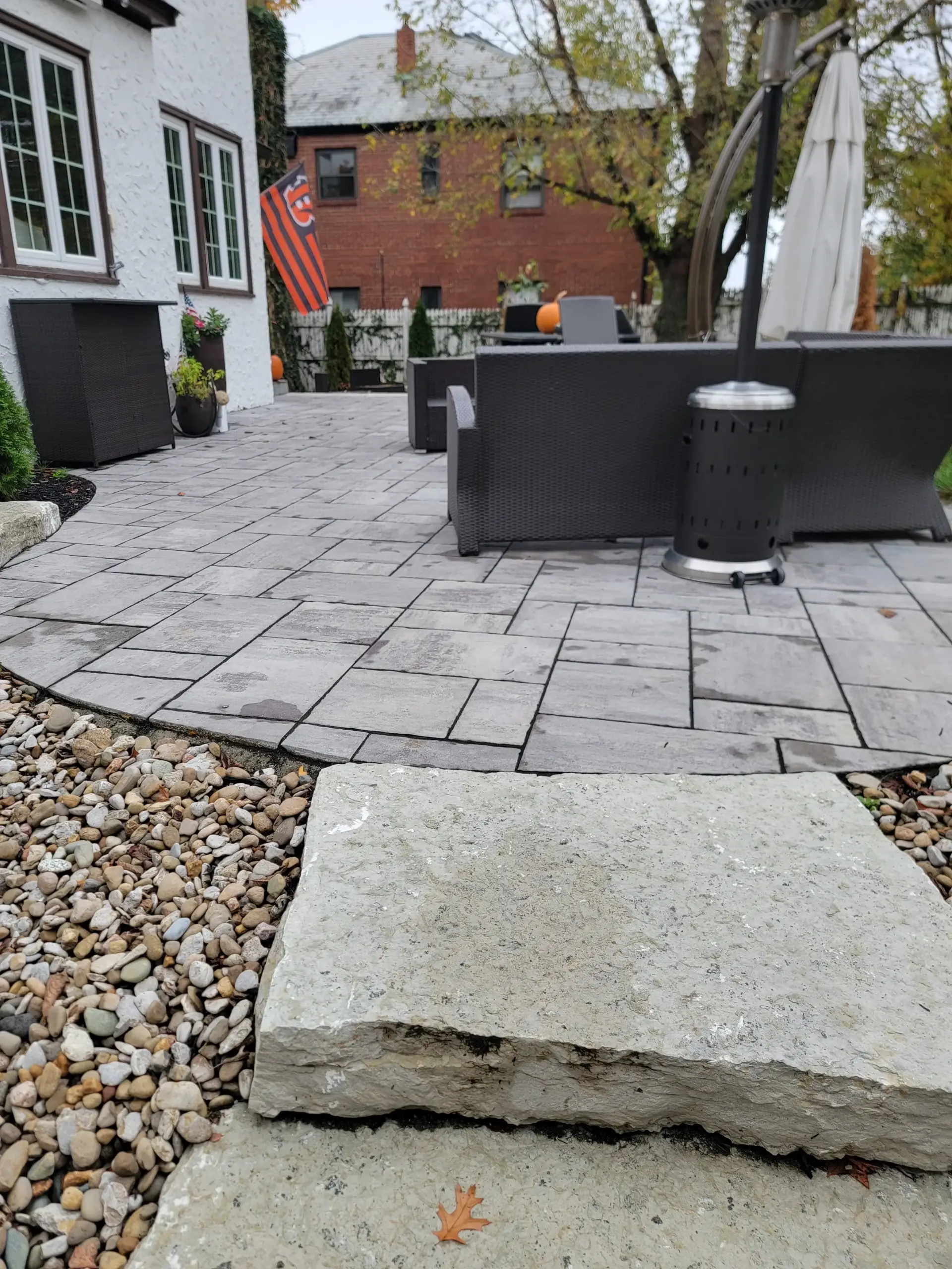 Stone-paved patio with dark wicker seating, a closed umbrella, patio heater, plants, and pumpkins