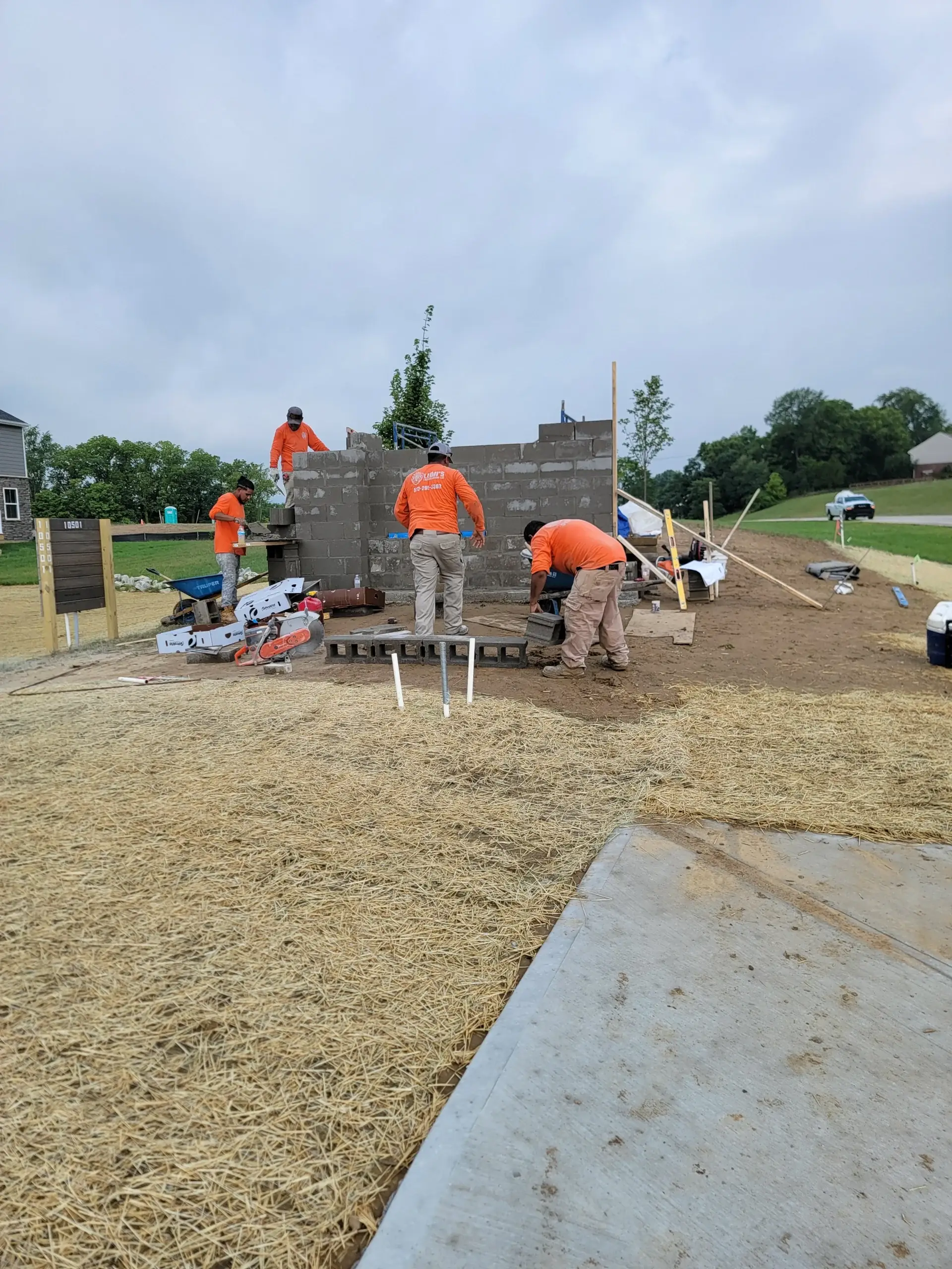 Crew building a concrete block wall beside a residential driveway