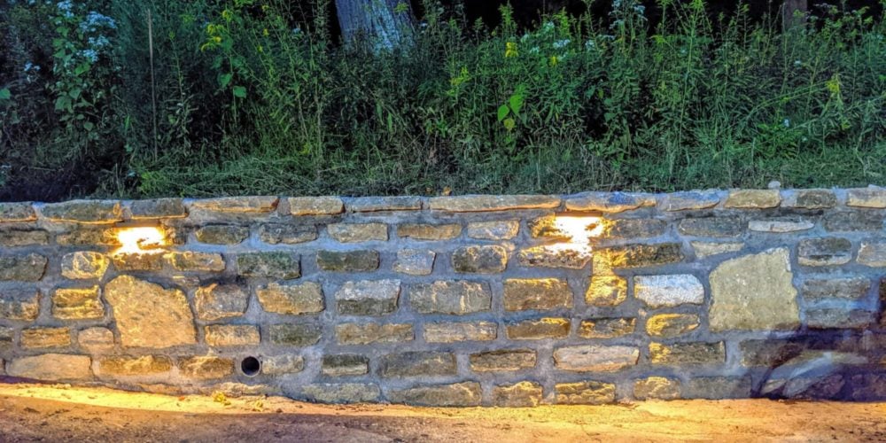 Stone retaining wall with integrated lights and dense plants at night